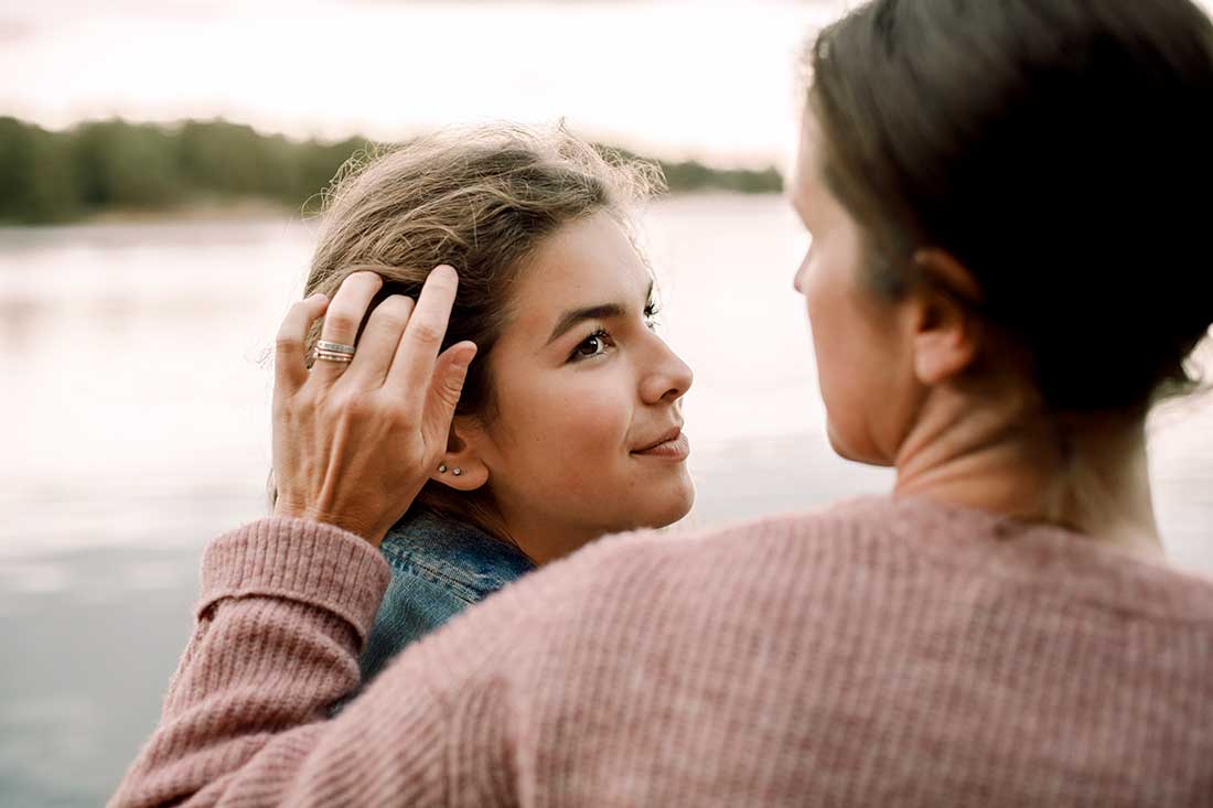 En vuxen kvinna drar sin hand genom en ung tjejs hår vid en strand